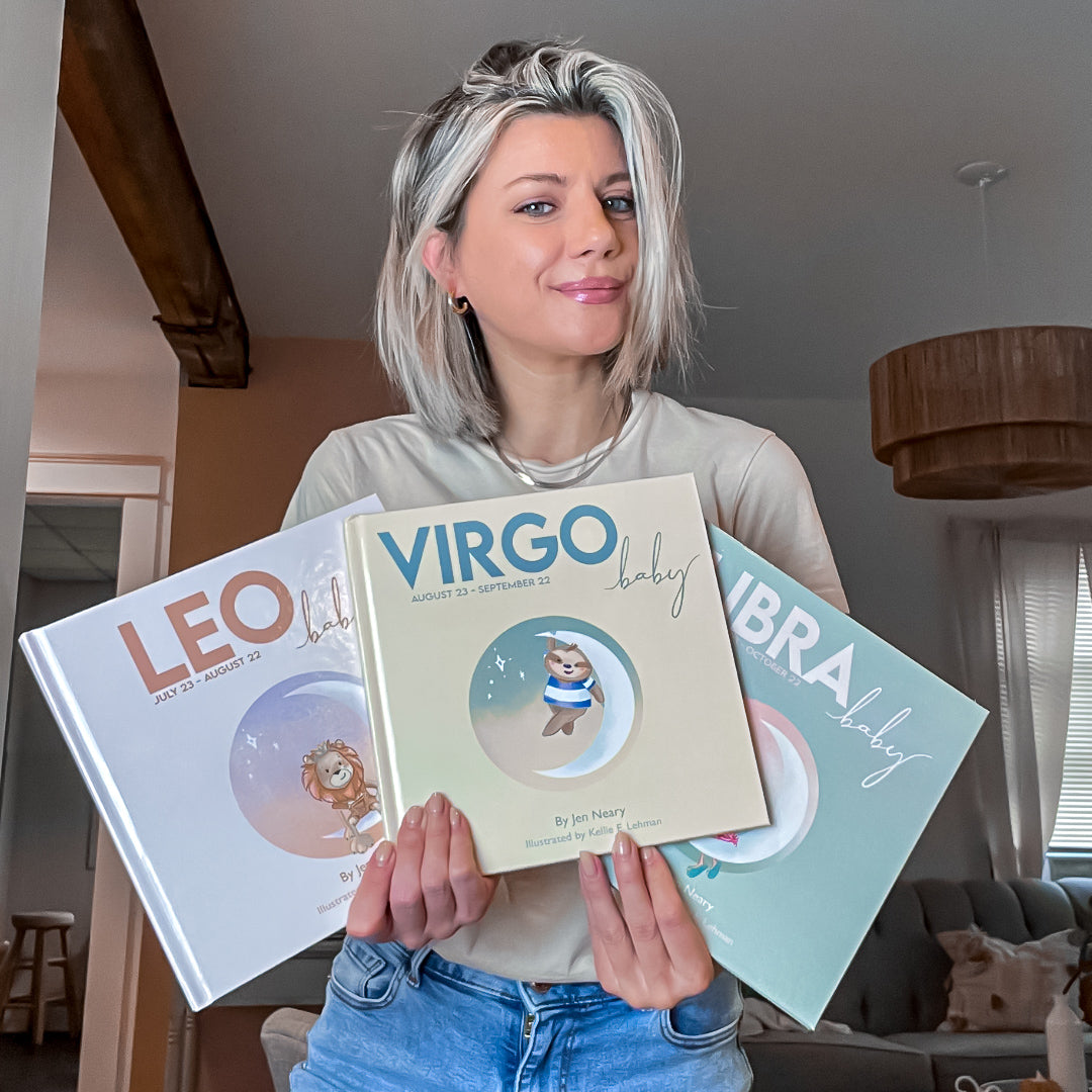 jen neary from zodiac baby posing with three of her books leo baby, virgo baby, and libra baby