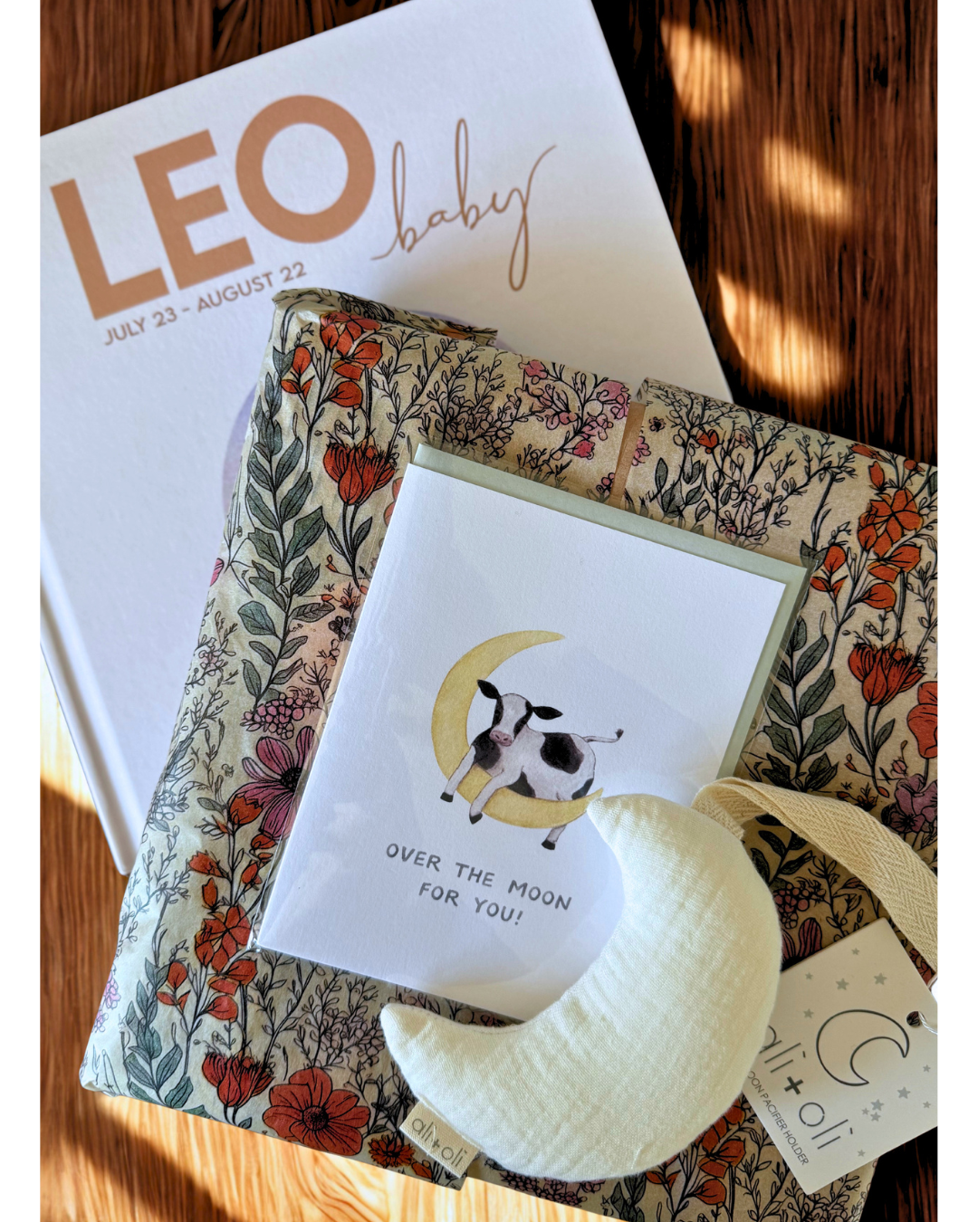 baby shower gift set for a leo baby featuring a zodiac baby book moon pacifier holder and over the moon new baby greeting card